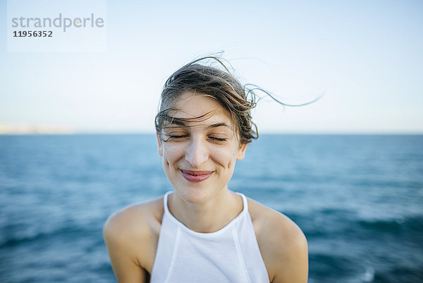 Junge Frau lächelnd mit geschlossenen Augen und Meereshintergrund
