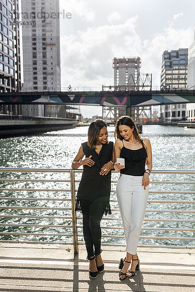Zwei Frauen auf einer Brücke teilen sich ein Handy in der Stadt.