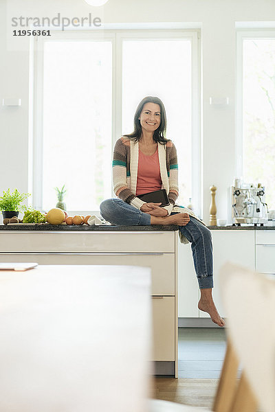 Porträt einer lächelnden Frau zu Hause  die auf der Küchentheke sitzt