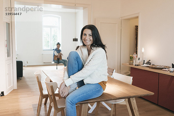 Porträt einer lächelnden Frau  die zu Hause auf dem Tisch sitzt.