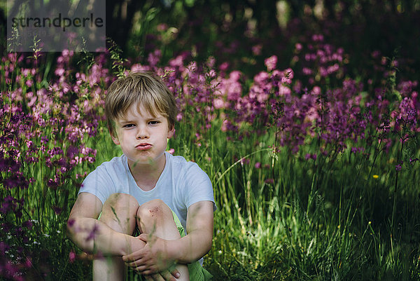 Porträt eines kleinen Jungen  der auf einer Wiese im Garten sitzt und den Mund schmollt.