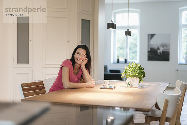 Porträt einer lächelnden Frau  die zu Hause am Tisch sitzt.