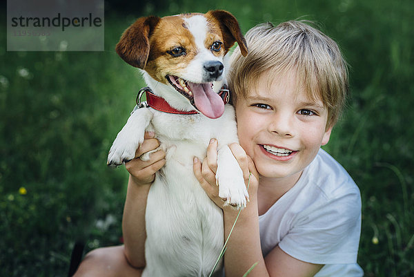 Porträt des glücklichen kleinen Jungen mit seinem Hund auf der Wiese im Garten