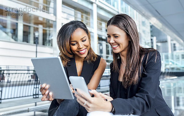 Zwei Geschäftsfrauen arbeiten mit Smartphone und Tablet in der Stadt