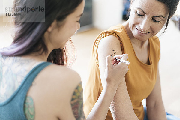 Frau malt Tattoo auf Arm einer anderen Frau