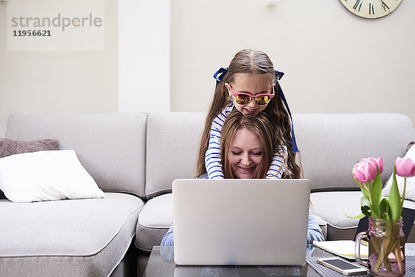 Porträt von lächelnder Mutter und kleiner Tochter mit Laptop im Wohnzimmer