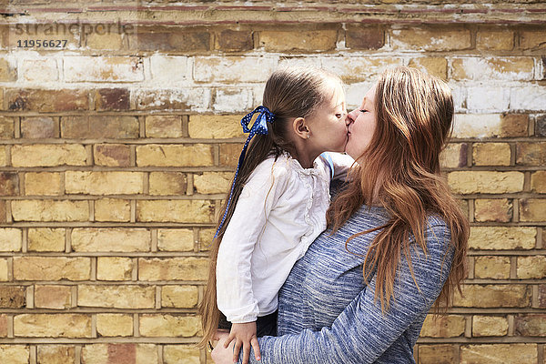 Mutter küsst ihre kleine Tochter vor der Backsteinmauer