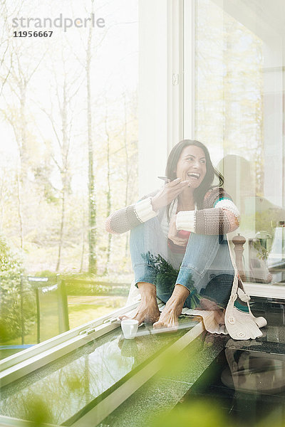 Lachende Frau zu Hause auf der Fensterbank sitzend