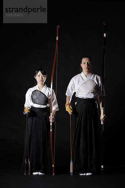 Multiethnische traditionelle japanische Kyudo-Bogenschützen auf schwarzem Hintergrund