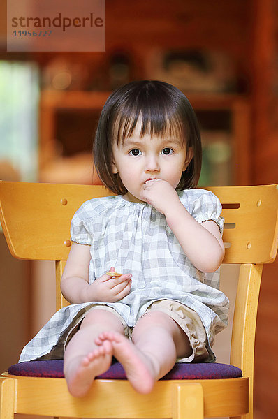 Gemischtrassiges junges Mädchen isst auf einem Holzstuhl