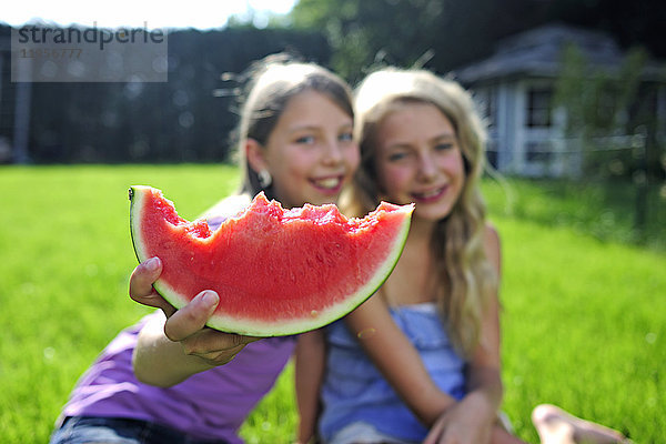 Zwei glückliche Mädchen beim Essen einer Wassermelone im Garten