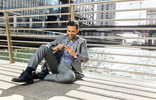 Geschäftsmann sitzend auf einer Brücke mit Handy in der Stadt