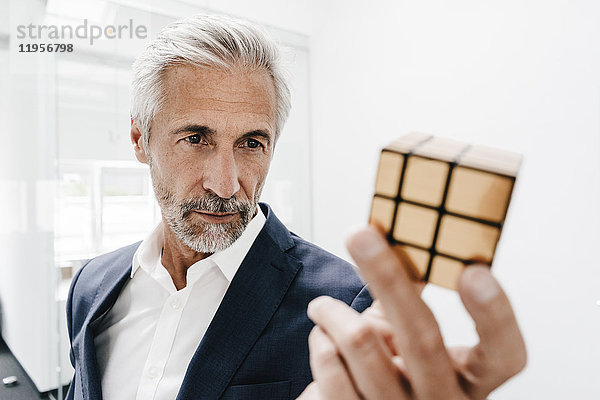 Der reife Geschäftsmann im Büro untersucht Rubik's Cube