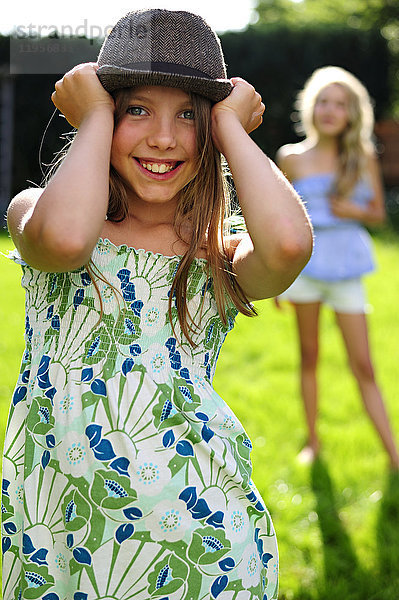 Glückliches  verspieltes Mädchen  das einen Hut im Garten aufsetzt.