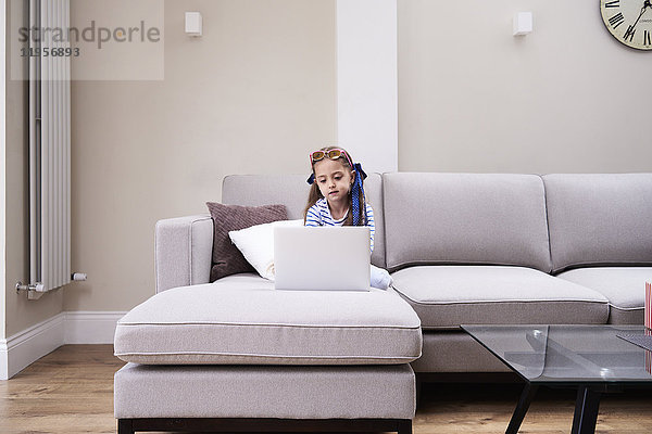 Kleines Mädchen auf der Couch mit Blick auf den Laptop