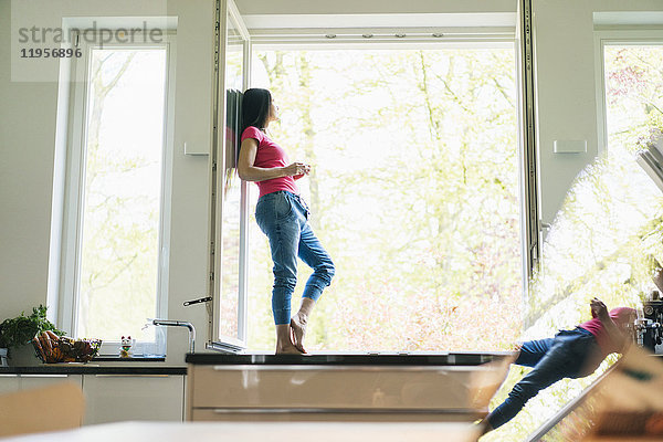 Frau steht in der Küche auf der Fensterbank