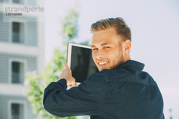 Porträt eines lächelnden jungen Mannes beim Fotografieren mit Tablette
