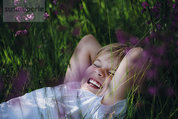Lachender kleiner Junge liegt auf einer Wiese im Garten.