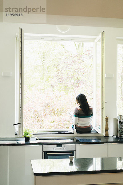 Frau in der Küche auf der Fensterbank sitzend