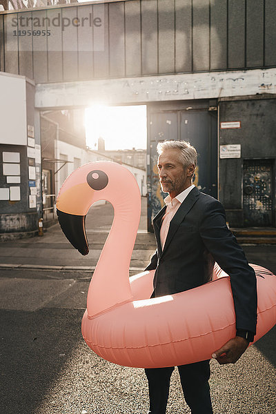 Erwachsener Geschäftsmann auf der Straße mit aufblasbarem Flamingo