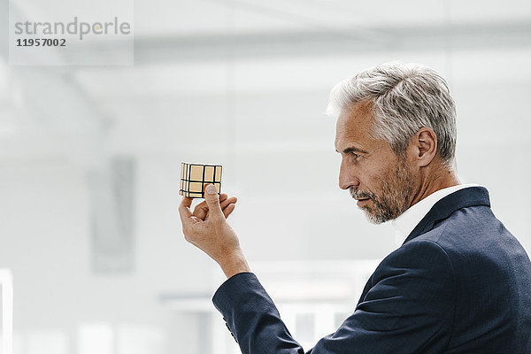 Der reife Geschäftsmann im Büro untersucht Rubik's Cube