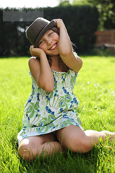 Fröhliches verspieltes Mädchen mit Hut im Garten sitzend