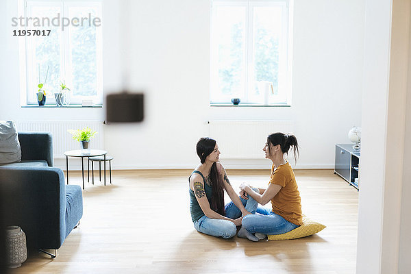 Zwei Frauen  die zu Hause auf dem Holzboden sitzen und reden.
