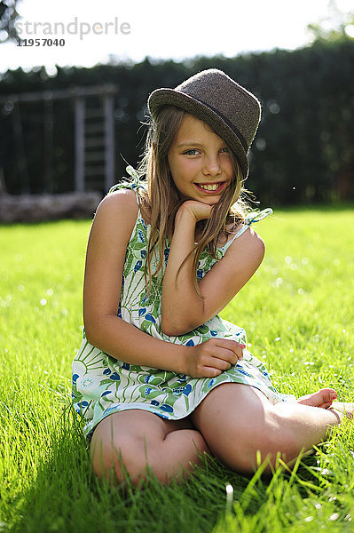 Lächelndes Mädchen mit Hut im Garten sitzend