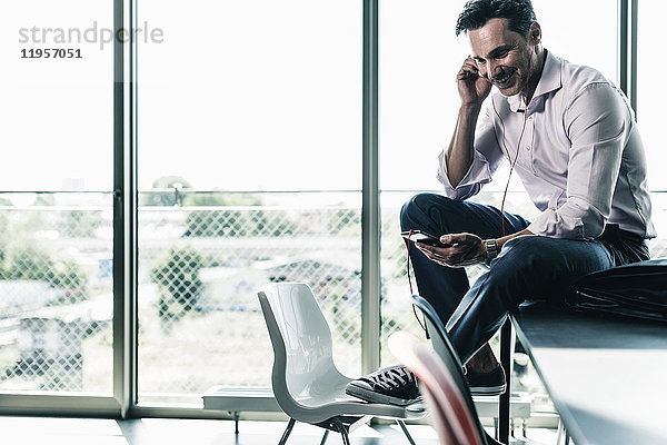 Geschäftsmann im Büro auf dem Schreibtisch sitzend  mit Smartphone