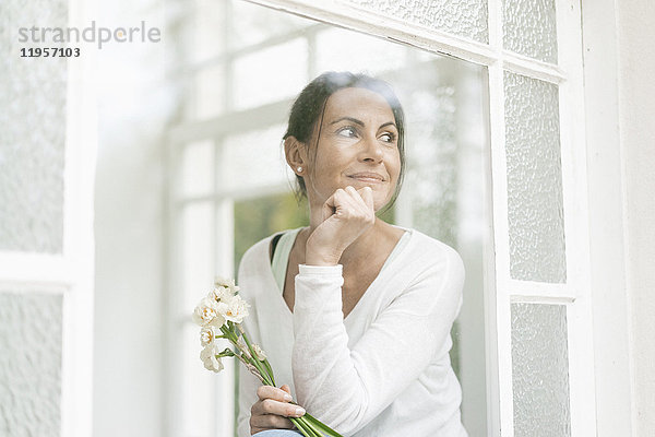 Lächelnde Frau mit Blumen aus dem Fenster