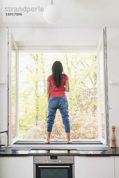 Frau steht in der Küche auf der Fensterbank