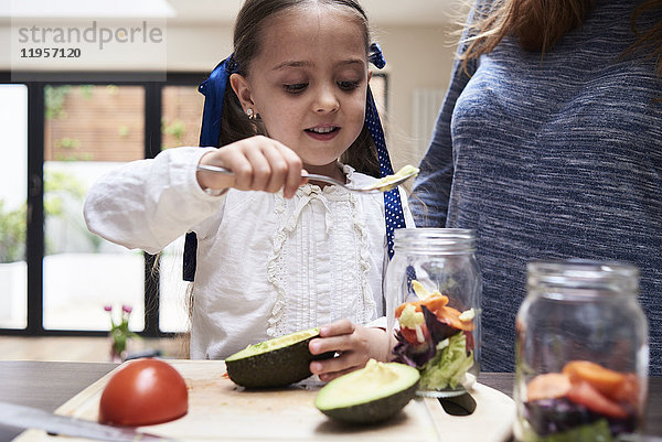 Porträt eines kleinen Mädchens  das mit seiner Mutter in der Küche einen gesunden Salat zubereitet.