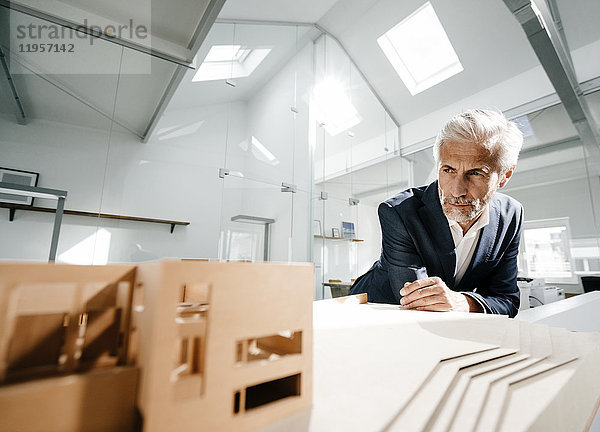 Ausgereifter Geschäftsmann untersucht Architekturmodell im Büro