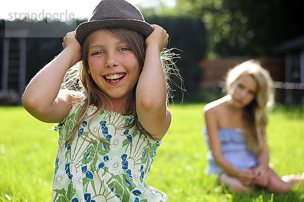 Glückliches  verspieltes Mädchen  das einen Hut im Garten aufsetzt.