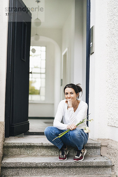 Frau mit Blumen auf der Türschwelle sitzend