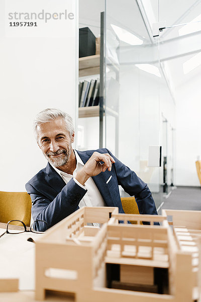 Porträt eines lächelnden Geschäftsmannes mit Architekturmodell im Büro