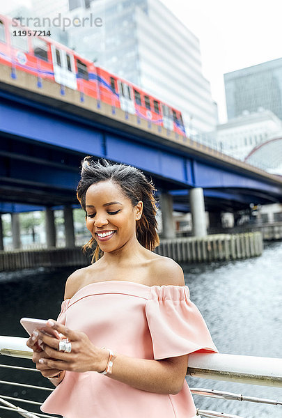 Lächelnde Frau sendet Nachrichten mit ihrem Smartphone in der Stadt