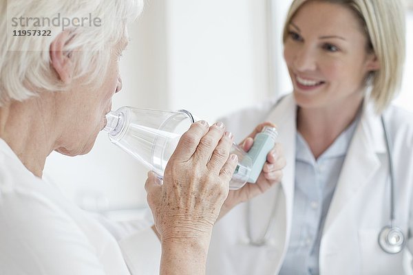 MODELL FREIGEGEBEN. Ältere Frau  die einen Inhalator benutzt  während eine Ärztin zusieht.