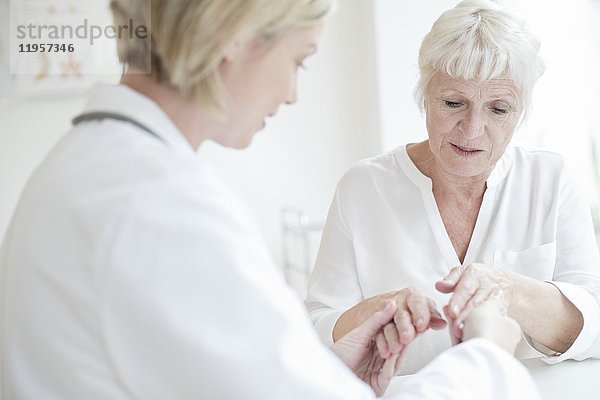 MODELL FREIGEGEBEN. Eine Ärztin untersucht die Hand eines älteren Patienten.