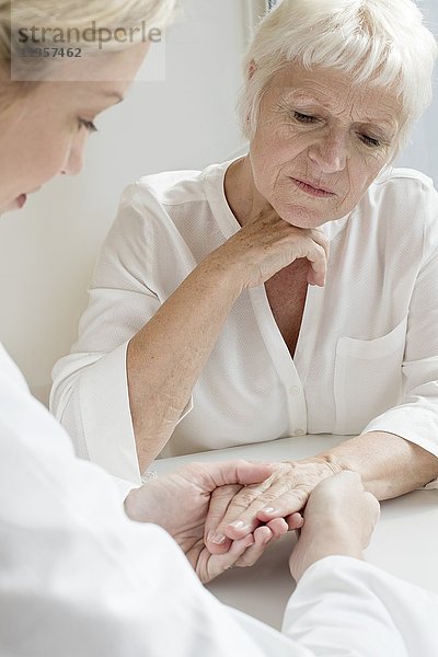 MODELL FREIGEGEBEN. Eine Ärztin untersucht die Hand eines älteren Patienten.