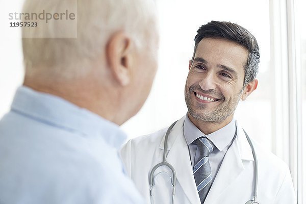 MODELL FREIGEGEBEN. Männlicher Arzt  der einen älteren Patienten anlächelt.