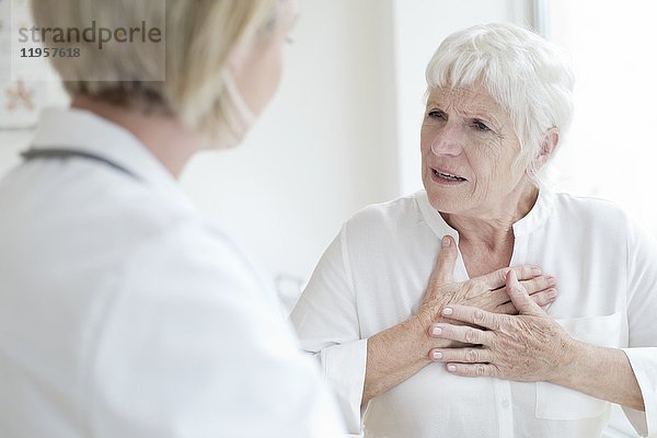 MODELL FREIGEGEBEN. Ältere Frau berührt die Brust und spricht mit einer Ärztin.