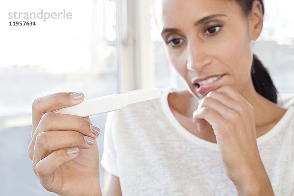 Mittlere erwachsene Frau mit Schwangerschaftstest in der Hand  besorgt.