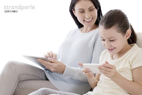 Mutter und Tochter auf dem Sofa mit digitalem Tablet und Smartphone.