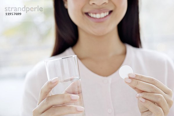 Junge Frau mit Tablette und Glas Wasser in der Hand.