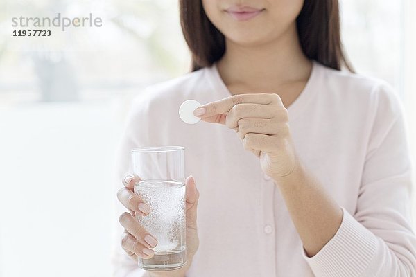 Junge Frau mit Tablette und Glas Wasser in der Hand.