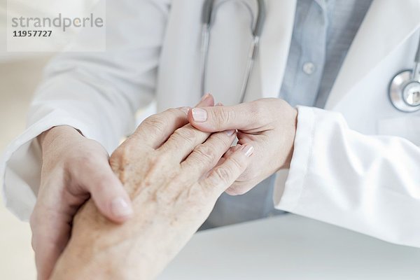 MODELL FREIGEGEBEN. Eine Ärztin hält die Hand eines älteren Patienten.