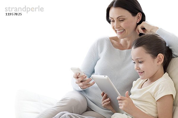 Mutter und Tochter auf dem Sofa mit digitalem Tablet und Smartphone.