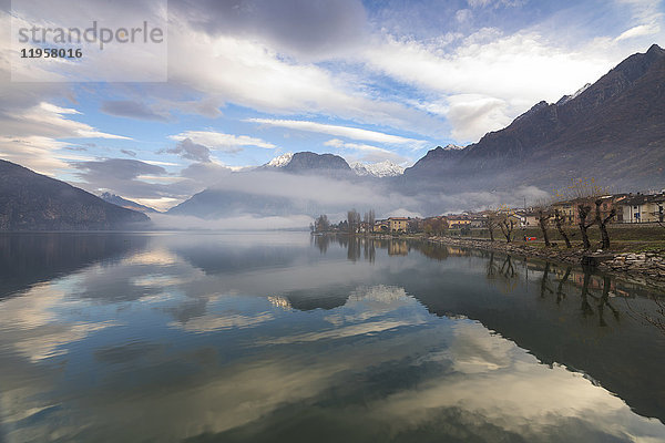 Berge und Dorf spiegeln sich im nebelverhangenen Mezzola-See in der Morgendämmerung  Verceia  Chiavenna-Tal  Lombardei  Italien  Europa