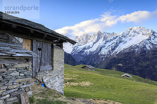 Alphütte umrahmt von Wiesen und verschneiten Gipfeln in der Morgendämmerung  Tombal  Soglio  Bergell  Kanton Graubünden  Schweiz  Europa